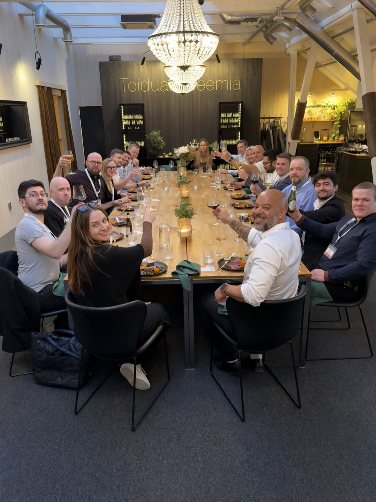 Guests at an Astra private dinner raising their glasses around a long candlelit table beneath a chandelier.